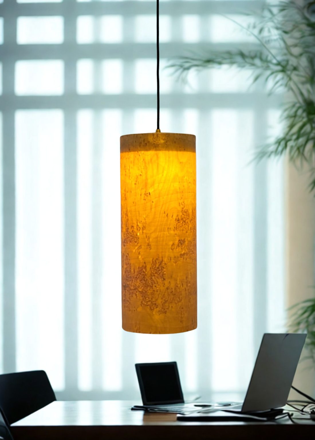 Nordic Birch Glow pendant lamp lit above a desk, its curly birch figure glowing amber