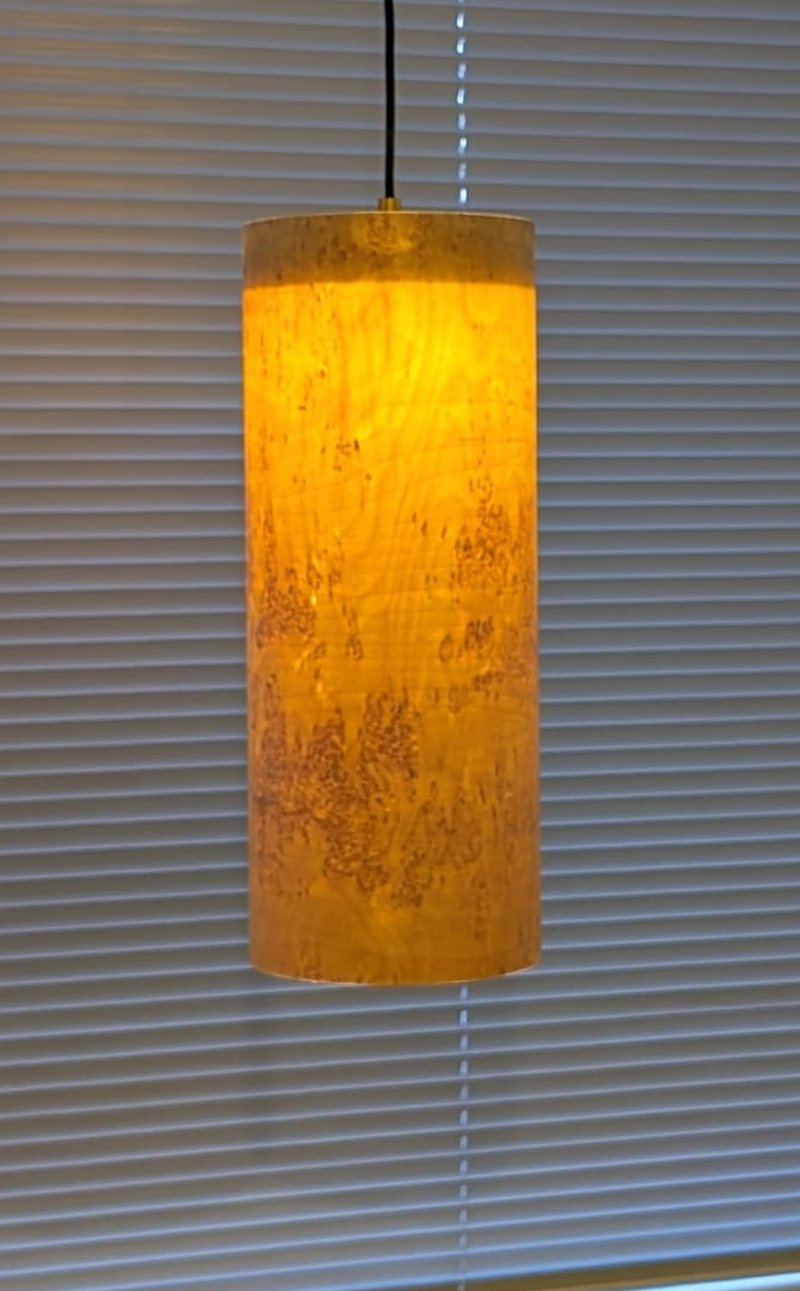The same lamp switched on: the curly birch figure glows amber